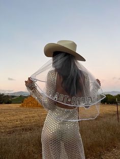 a woman in a white dress and cowboy hat is holding up a veil with the word astro written on it