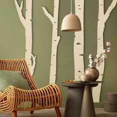 a wicker chair and table in front of a wall with trees painted on it