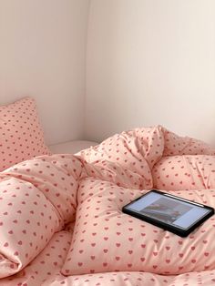 a bed with pink and white hearts on the comforter, pillows and an electronic device