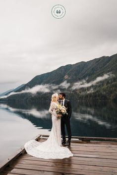 a bride and groom standing on a dock in front of a mountain lake with fog