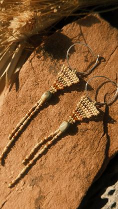 two beaded earrings sitting on top of a rock next to some feathers and beads