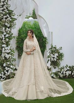 a woman wearing a wedding gown and veil standing in front of an archway with white flowers