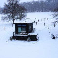 a small cabin in the middle of a snowy field with chairs and tables around it