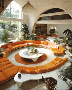 a living room filled with orange couches and lots of plants on top of it