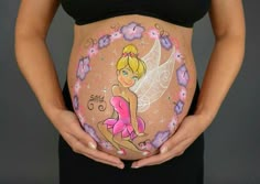 a pregnant woman holding her belly painted with flowers and a fairy tinkerbell on it