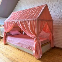 a pink canopy bed in a room with white brick walls and wooden floors, along with hardwood flooring