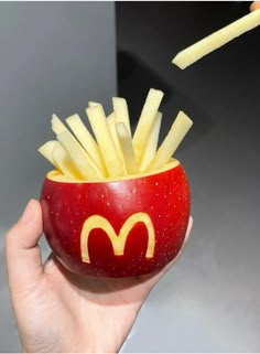 a hand holding a red apple with french fries in the shape of a mcdonald's logo