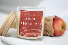 an apple pie candle sits next to some apples