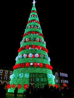 a large christmas tree is lit up in green and red with people standing around it