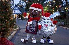 two people in costumes standing next to each other on the street with christmas lights behind them