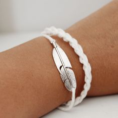 a woman's arm wearing a white bracelet with a feather charm on the clasp