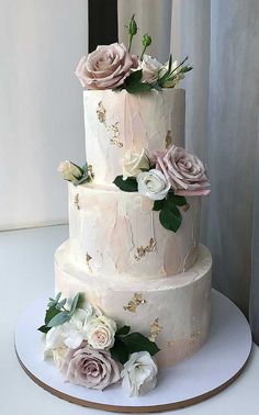 a three tiered wedding cake with pink and white flowers on the top, sitting on a table