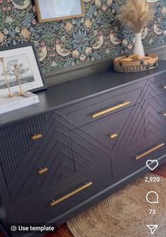 a black dresser with gold trim and some pictures on the wall behind it in a room