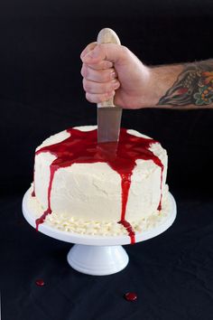 a man is holding a knife over a cake with white frosting and red sauce on it