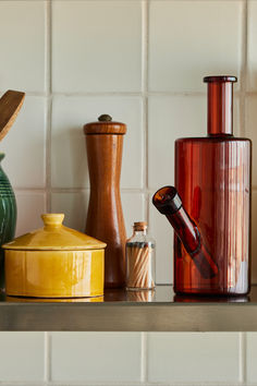 several vases and jars on a shelf in a room with white tile backsplash