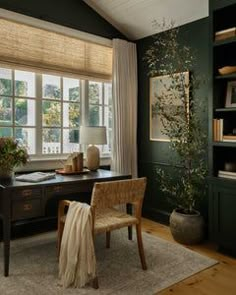 a home office with green walls and wooden floors, along with a large window covered in blinds