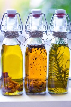 three glass bottles filled with different types of liquid and plants on a window sill