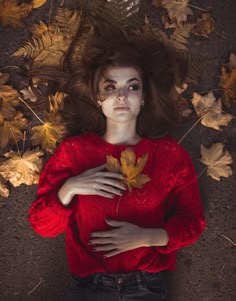 a woman laying on the ground with her hands in her chest and leaves around her