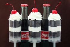 three coke bottles with whipped cream and cherries in them