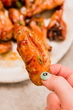 a hand holding up a piece of chicken wings with sauce on it's side