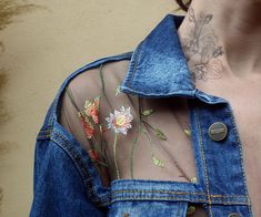 a woman wearing a jean jacket with flowers embroidered on the chest and behind her is a tattoo