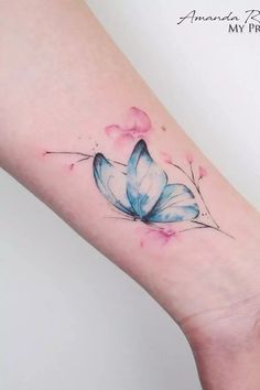 a blue and white butterfly tattoo on the left arm, with pink flowers around it