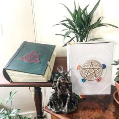 a table topped with books and a statue next to a potted plant on top of it