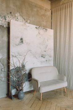 a white chair sitting in front of a painting on the wall next to a plant