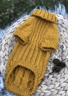 a yellow knitted mitt laying on top of a basket next to pine cones