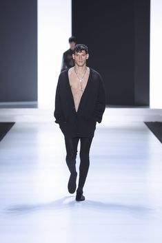 a man walking down a runway wearing a black shirt and pants with no shirt on