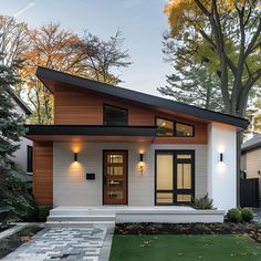 This stylish Scandinavian bungalow features a striking sloped roof and a blend of white stucco and wood siding. Large windows and a sleek door, flanked by minimalist wall lights, enhance the modern facade. The front yard boasts a paved walkway and a lush lawn, complementing the clean lines and natural materials. This design beautifully merges traditional Scandinavian elements with contemporary architecture, making it a perfect blend of elegance and modernity. Two Story Slanted Roof House, One Side Roof House Design, White House With Wood Posts, White And Wood Modern House, House Design Wood Modern, Skillion Roof Facade Modern Exterior, Country Home Designs Exterior, White House Natural Wood Trim Exterior, Modern House Exterior Materials