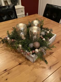 a wooden table topped with silver cups and christmas decorations on top of it, surrounded by greenery