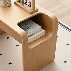 a small wooden table with a clock on it and books in the drawer next to it