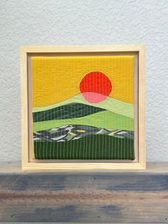 a painting on a wooden shelf with a white wall behind it and a red sun in the background