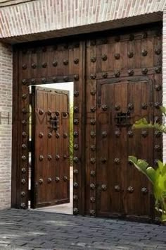 two large wooden doors are open in front of a brick building with a plant on the sidewalk