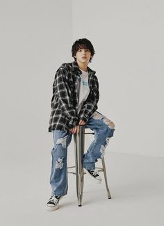 a young man sitting on top of a stool wearing ripped jeans and a plaid shirt