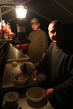 two men are preparing food in the kitchen at night, while another man is standing next to them