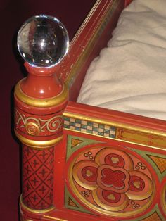 a red and gold bed frame with a glass ball on the headboard, in front of a white pillow