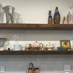 two wooden shelves above a kitchen sink filled with cups and saucers on top of it