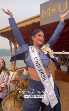 a woman wearing a blue top and pants with her arms in the air while standing on a boat