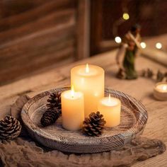 three lit candles on a tray with pine cones