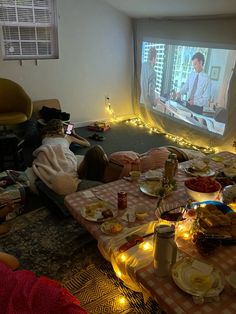 people are sitting on the floor watching tv and eating food in front of them,