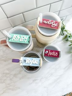 three coffee mugs with name tags on them sitting on a counter next to a potted plant