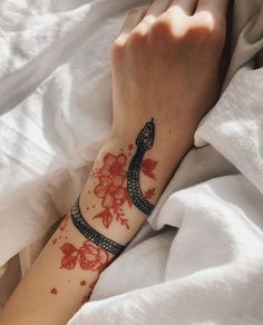 a woman's arm with a snake tattoo on it and flowers around the wrist