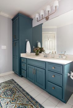 a bathroom with blue cabinets and white counter tops, rugs on the floor in front of it