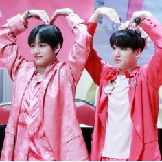 two young men standing next to each other in front of a pink wall holding their hands up