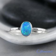 This Sterling Silver Blue Opal Ring features an 8 mm x 6 mm oval lab grown Blue Opal cabochon that has been securely set in a highly polished fine silver bezel. The band is made of a sturdy round Sterling Silver wire that has a hammered texture around the entire band. These beautiful rings make unique promise rings, lovely stacking rings, great birthstone rings, or just a wonderful love tokens for yourself or your special someone.This man-made Blue Opal is created from very uniform nanoparticles Oval Opal Rings With Bezel Setting, Classic Blue Oval Opal Ring, Classic Blue Opal Ring As A Gift, Classic Blue Opal Ring As Gift, Classic Blue Opal Ring For Gift, Classic Blue Opal Ring Gift, Blue Cabochon Opal Ring, Blue Cabochon Opal Ring For Anniversary, Blue Oval Opal Ring With Polished Finish