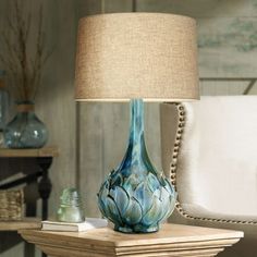 a blue vase sitting on top of a wooden table next to a white chair and lamp