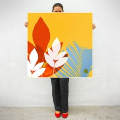 a woman holding up a large painting with leaves on it in front of a white wall