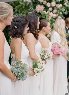 a group of women standing next to each other in white dresses holding bouquets and flowers